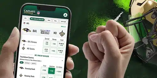 A person in Kansas using the Caesars Sportsbook mobile app to build an NFL parlay for the Ravens vs. Saints game, with a fist pump celebrating a potential win.